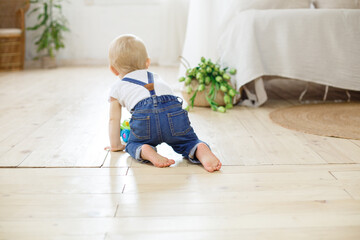 Little boy sitting on a wooden floor , scandinavian interior. Infant boy weared in casual denim. Small baby feet. Kid of one year old crawls on the floor. Small legs. First birthday