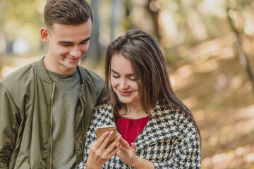 Fototapeta premium Leisure and technology concept. Smiling friends with smartphone standing in park, watching some media together.