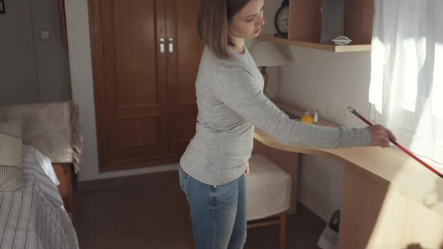 Young woman cleaning with a feather duster in bedroom