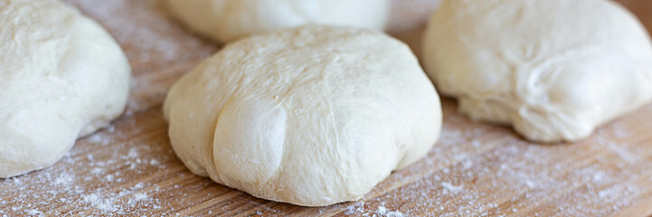 A round pieces of homemade white dough for pizza, bread or baking goods on a wooden cutting board. Small pieces of dough ready to be baked. Healthy natural family food. Side view, daylight, home 