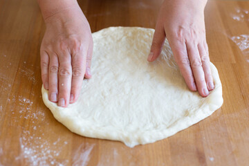 Wooman is making homemade pizza for the family. Hands of a woman roll out the dough in the home kitchen, daylight. The process of making fresh homemade elastic dough for baking pizza or pie. Easy cook