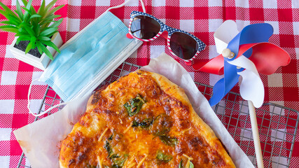 Picnic for Independence Day the USA. Homemade pizza cooked by a child on a red tablecloth, sunglasses with the flag of America and a medical mask. Daylight.
