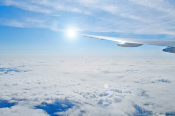 Airplane wing out of window, flying above the morning clouds