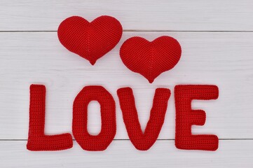 Red knitted hearts and the word love are placed on white wooden boards.