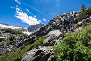 Blonde woman hiker with a backpack navigates and does rock scambling along the 20 Lakes Basin trail