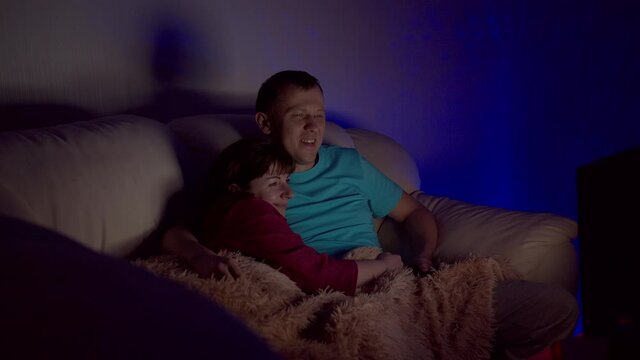 Married couple sitting embracing late at night and watching TV