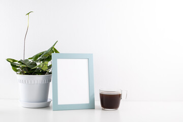 Blank wooden picture frame with a cup of black coffee and potted house plant on a table, white wall background.