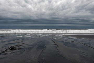 Dark storm clouds in the sky over the sea. Black sand beach with small river. Storm cyclone over the ocean. Weather warning. Forces of nature
