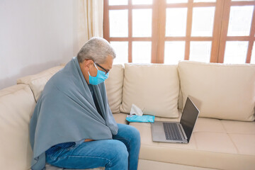 Profile view of a man with a surgical mask having an online consultation with his doctor while sick with covid19 coronavirus and remaining isolated at home