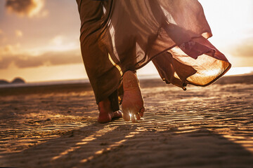 Nahaufnahme von Frauenfüßen, die bei Sonnenuntergang am Strand spazieren gehen