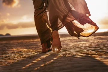 Fototapeten Nahaufnahme von Frauenfüßen, die bei Sonnenuntergang am Strand spazieren gehen © zolotareva_elina