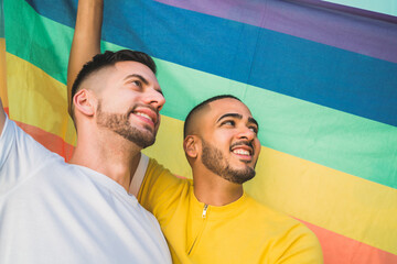 Gay couple embracing and showing their love with rainbow flag.