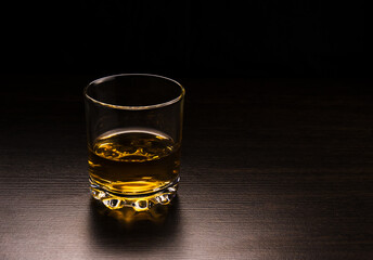 A glass with a whiskey table made of dark wood on a dark background.