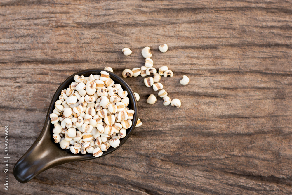 Wall mural Closeup white Job's tears ( Adlay millet or  pearl millet ) in black ceramic bowl isolated on wood table background,Top view. Flat lay