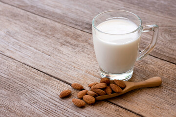 Glass of Almond milk and almond seeds in wooden scoop isolated on wood table background. Healthy drinks concept.