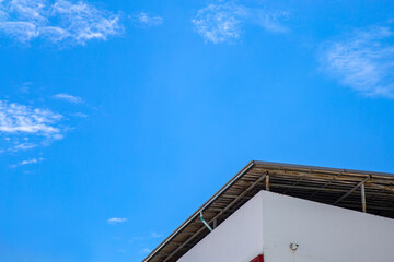 Low angle picture a corner roof on a building against blue sky with clouds in summer.