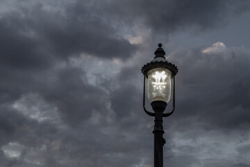 Fototapeta na wymiar Old fashioned illuminated lamp post set against a dark cloudy sky in horizontal orientation with copy space.