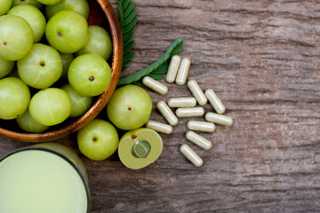 Close-up fresh organic green Amla or Indian gooseberry fruits ( phyllanthus emblica ) with capsules and glass of gooseberry juice tea isolated on rustic wood table background. Overhead view. Flat lay.