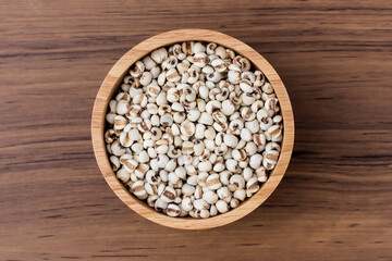 Close-up white Job's tears ( Adlay millet, pearl millet or coix seeds ) in wooden bowl and scoop isolated on wood table background. Overhead  view. Flat lay.