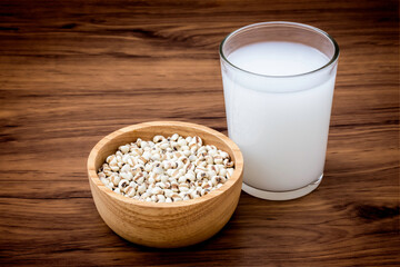 Closeup white Job's tears ( Adlay millet or pearl millet ) in wooden bowl and glass of fresh millet milk isolated on wood table background. 
