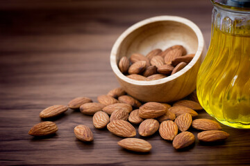Closeup sweet Almond nut seeds in wooden bowl with bottle of extracted essential almonds oil on wood table background. Selective focus. Vintage tone.