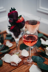 Glasses of rose wine surrounded by petals with chocolate covered strawberries