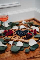 Berry Charcuterie Tray with a glass of rose surrounded by petals and leaves 