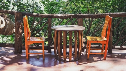Fototapeta na wymiar Wooden table and two wooden chairs Laid bare, no one sitting Arranged for sitting, relaxing or eating The area near the wooden fence in front of the house With trees and leaves Object background