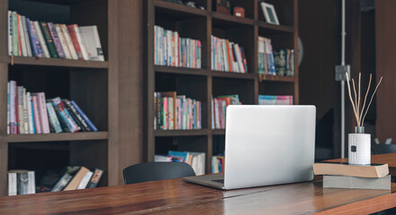 Laptop computer on wooden table in contemporary room with book shelf background. Copy space.