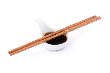 Tasty soy sauce in small ceramic bowl and wooden chopsticks isolated on white background. 