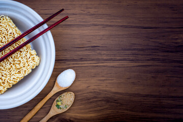 Raw instant noodles or dry noodle with monosodium glutamate (MSG ), ingredients in wooden spoon and medical stethoscope isolated on the wood table background. Unhealthy food concept. Top view.