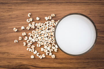 Closeup glass of fresh millet milk  and white Job's tears ( Adlay millet or pearl millet ) seeds isolated on wood table background. Top view. Flat lay.