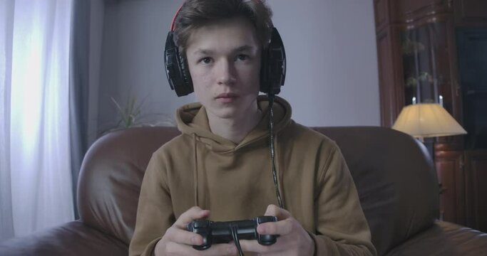 Young brunette boy on headphones and hoodie playing video game. Close-up portrait of Caucasian teenage guy having gaming addiction. Lifestyle, relaxation, leisure, Cinema 4k ProRes HQ.