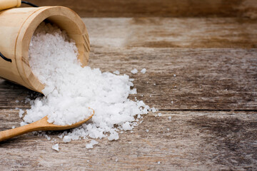Close up natural sea salt in wooden bucket and spoon splashing on old rustic wooden table background. 