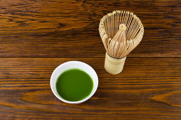 Bamboo matcha tea whisk also know as chasen with green matcha tea in a cup on a wooden background.
