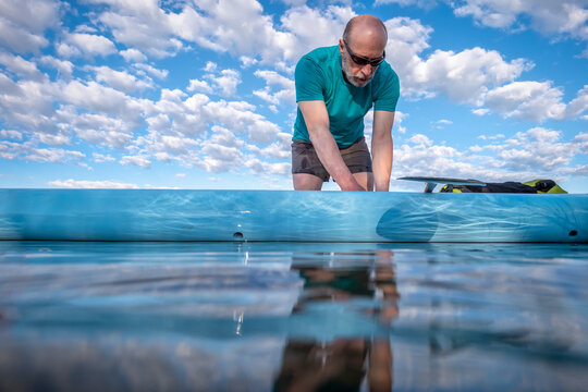 senior male paddler is preparing his stand up paddleboard for morning paddling workout, solo paddling as fitness and training with social distancing, low angle view from a partially submerged camera