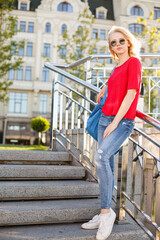 Beautiful girl walk in the summer Kiev City. Young woman tourist on street. Street style portrait. Stylish girl sitting on stairs weared in red casual outfit. Life style. Local tourism. Srteet walk. 