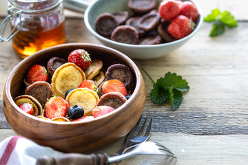 Different mini pancakes in a wooden bowl with honey and blueberries on a wooden table. Trendy food