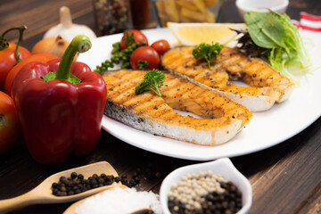 Delicious fillet cut salmon steak in white plate side dish with french fries and salad on dark wood background