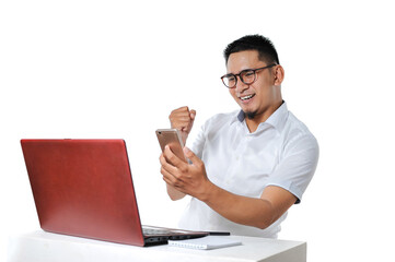 Portrait of excited Young Asian man sitting near laptop on the desk successfully completed the work as online freelancer