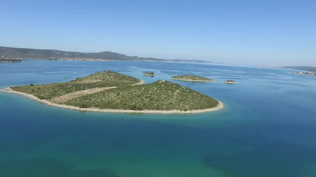 Aerial panning shot of small islands in blue sea against clear sky, drone ascending over water on sunny day - Biograd, Croatia
