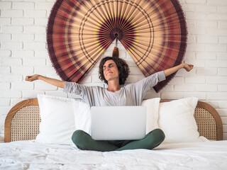 tired yawning exhausted lady in bed with laptop in Pajamas stretching her arms up at her bedroom in...