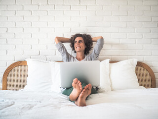 happy smiling relaxed woman in bed with laptop in Pajamas at her bedroom in home office
