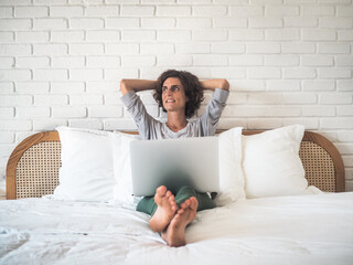 happy smiling relaxed woman in bed with laptop in Pajamas at her bedroom in home office
