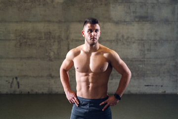 Fototapeta na wymiar Shirtless serious Caucasian man with hands on hips posing while standing in front of the wall.