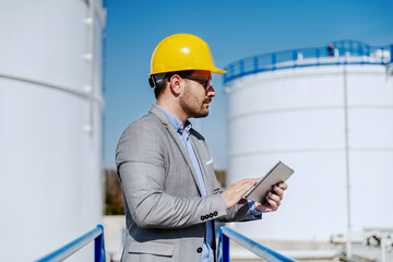 Side view of young attractive caucasian businessman in suit with helmet on head using tablet for...