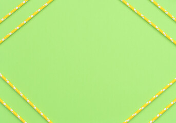 Green background with yellow paper straws on the corners. Drinking cocktail tubes. Eco-friendly concept. Flat lay with copy space for your text.