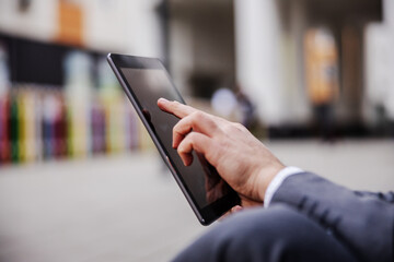 Closeup of man in suit sitting on the street and using tablet. Selective focus on hand.