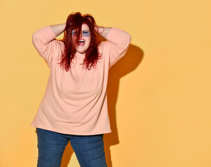 Young happy red haired overweight woman in casual clothing standing, shouting and tousling her hair