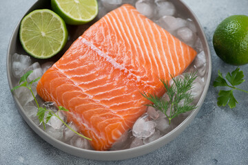 Round grey plate with raw fresh salmon fillet on ice, lime, dill and parsley, selective focus, horizontal 